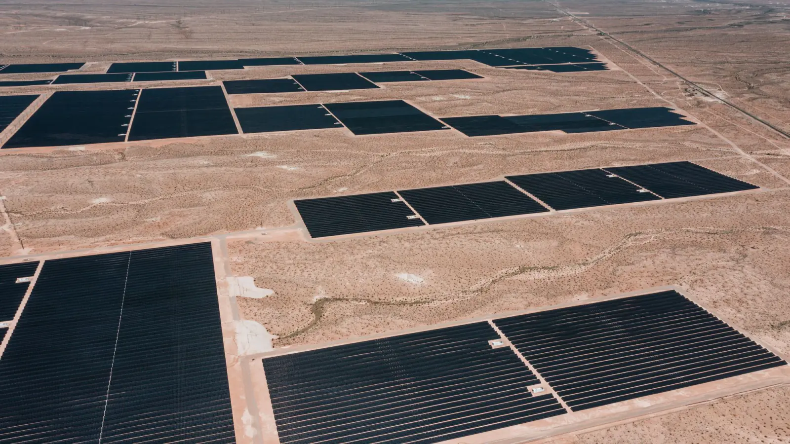 Aerial view of large blocks of solar modules spread across flat desert terrain