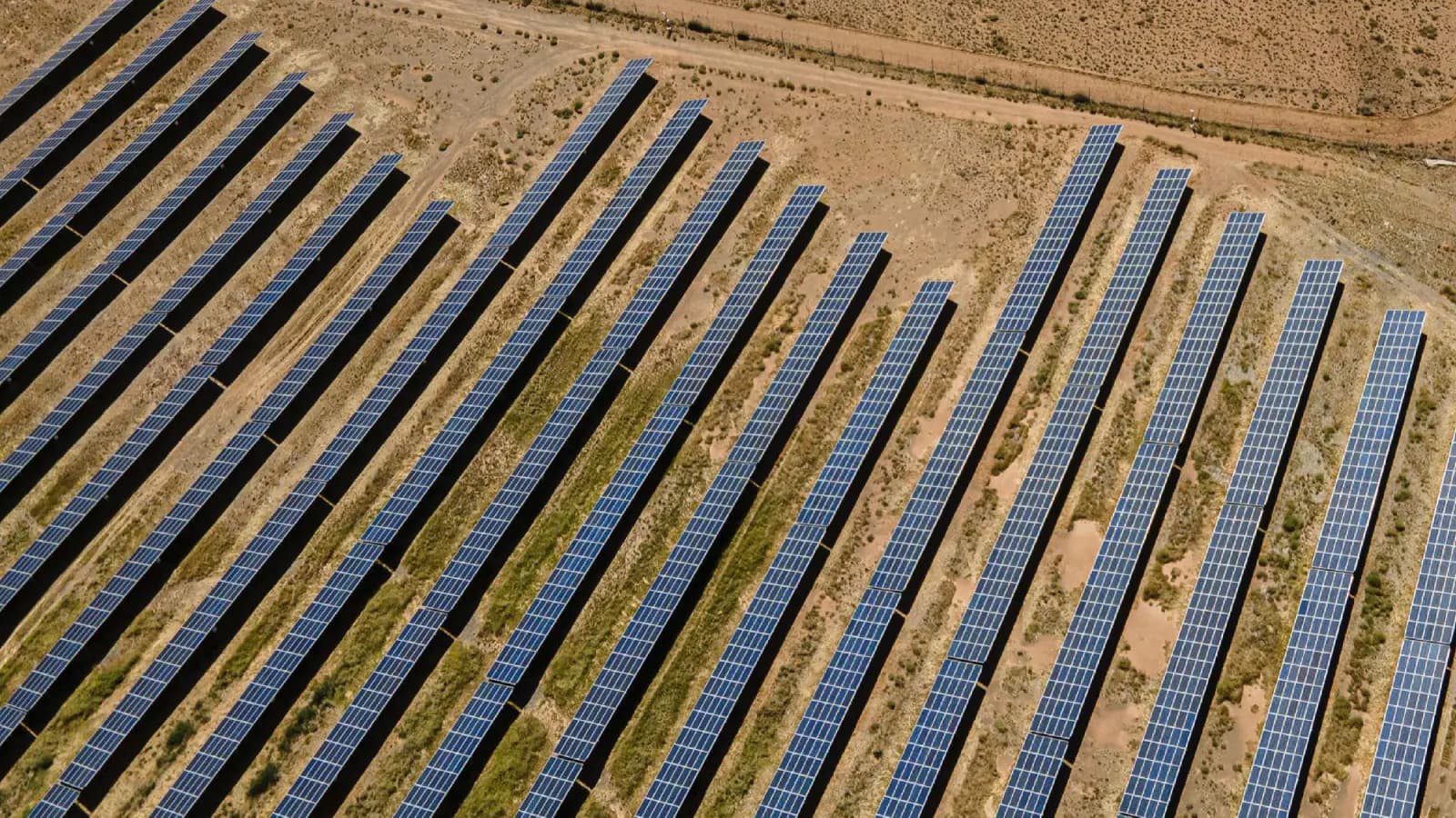 Aerial view of long rows of solar modules on mounting structures across dry, scrubby ground
